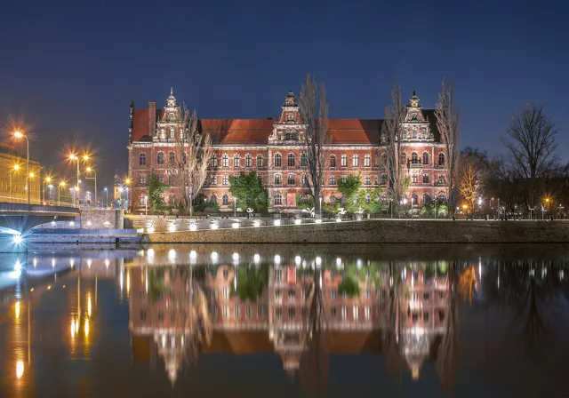 The National Museum in Wrocław, a red-brick building, reflected in the Oder at night