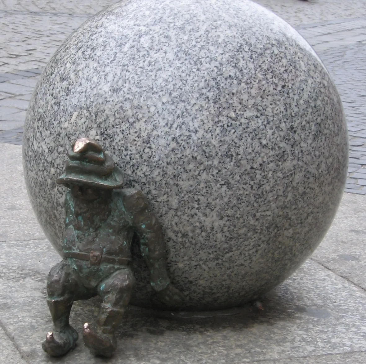 A bronze dwarf leaning against a big granite ball on a Wrocław street