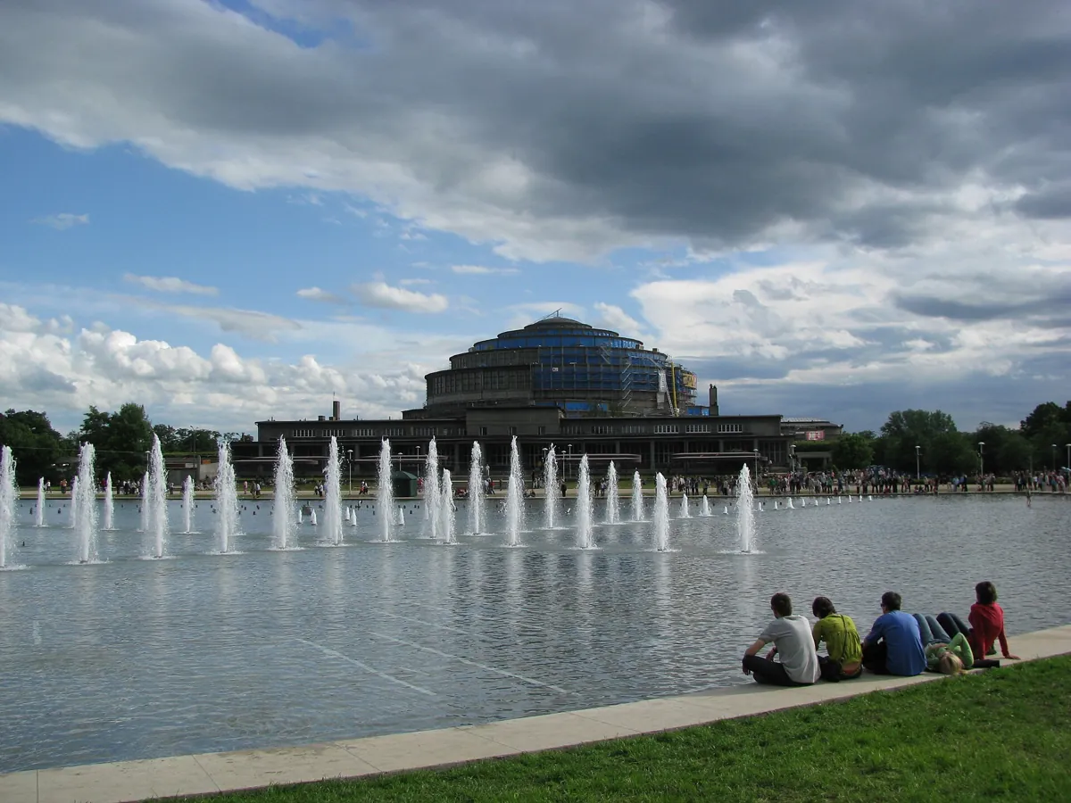Jets of the Multimedia Fountain in front of the Centennial Hall in Wrocław, with people sitting on the grass by the pool