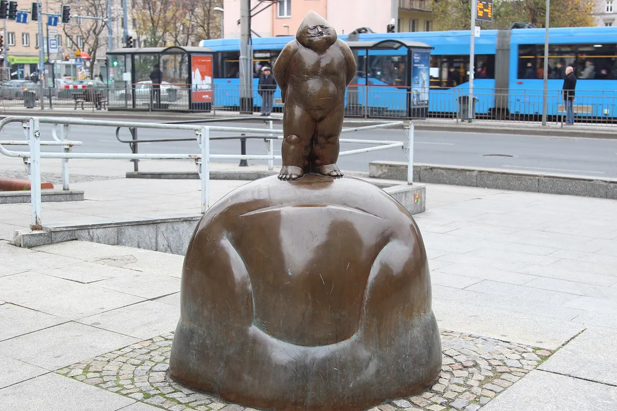 Papa Krasnal, the first bronze dwarf of Wrocław, standing on a rounded plinth near a tram stop